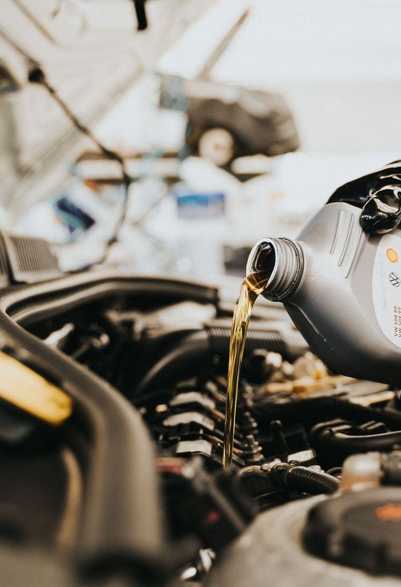 Close-up of a mechanic pouring engine oil into a car engine in an auto repair shop.